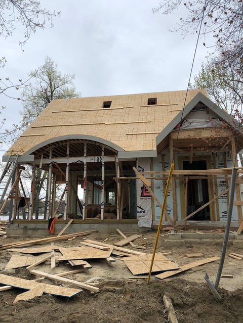 House under construction with new roof framing, wooden scaffolding, and building materials scattered on the ground