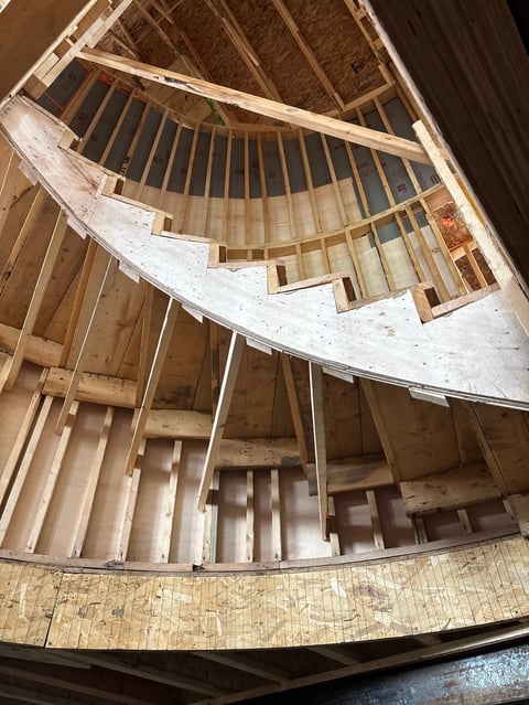 Interior view of a spiral staircase showing wooden steps spiraling upward from below, viewed from bottom looking up