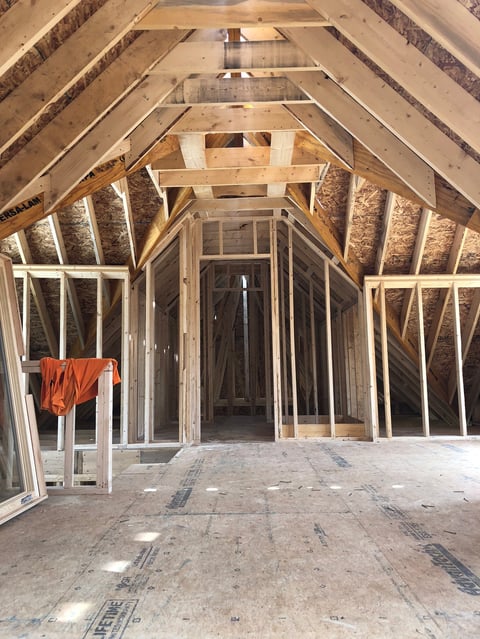 Interior of unfinished house under construction showing exposed wooden framing, studs, and rafters with orange cloth draped on ladder
