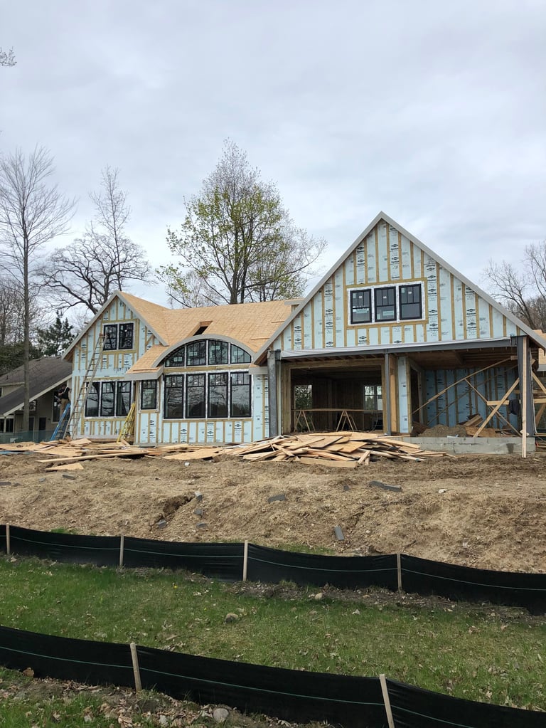 New house under construction with exposed framing, tan and white striped exterior, and bare dirt lot