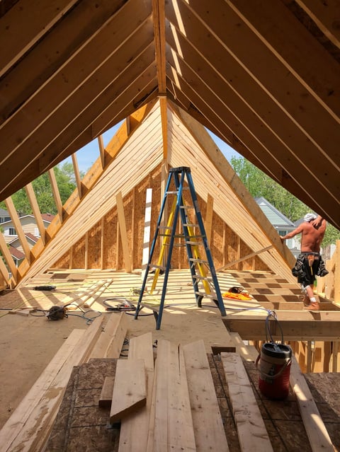 Interior of wooden house frame under construction with ladder, exposed beams, and worker in background