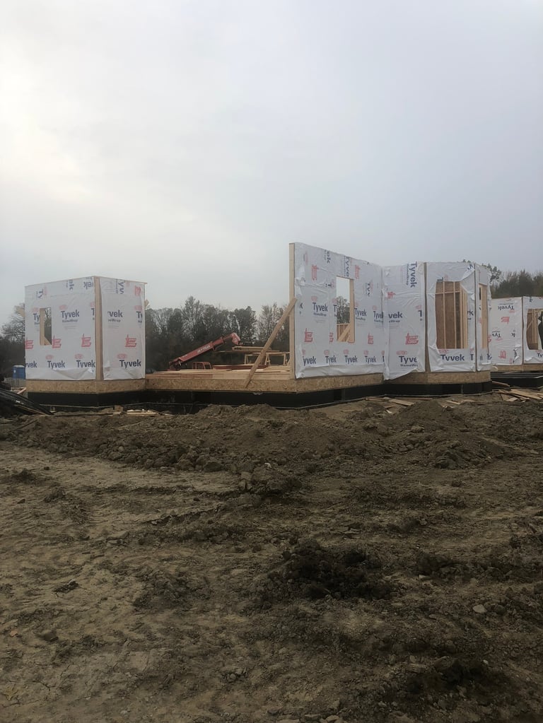 Construction site with wrapped building materials and wooden framing on dirt ground under overcast sky